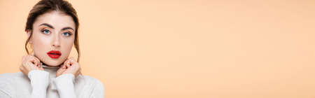 horizontal crop of stylish woman holding hands near face while looking at camera isolated on peach