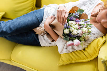 cropped view of young woman lying on yellow sofa with flowersの写真素材