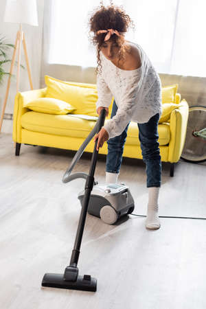 curly woman in socks using vacuum cleaner while cleaning homeの写真素材