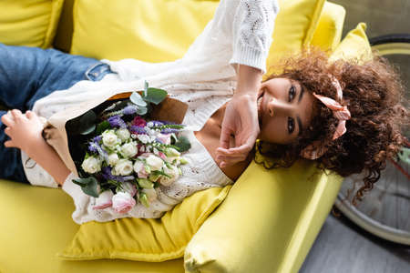 top view of curly woman with flowers laughing while lying on couchの写真素材
