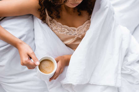 cropped view of woman holding cup with coffee in bedの写真素材