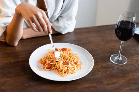 partial view of woman holding fork near plate with prepared spaghetti and glass of red wineの写真素材
