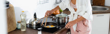 panoramic crop of woman cooking eggs on frying pan in kitchenの写真素材