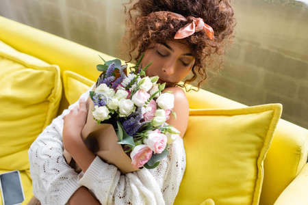 young woman with closed eyes holding bouquet and smelling flowers in living roomの写真素材