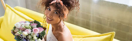 panoramic crop of pleased woman holding bouquet of flowers in living roomの写真素材