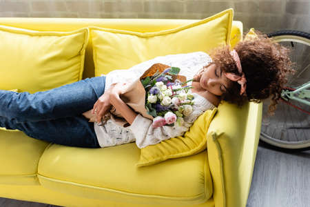 young curly woman with closed eyes lying on yellow sofa with flowersの写真素材