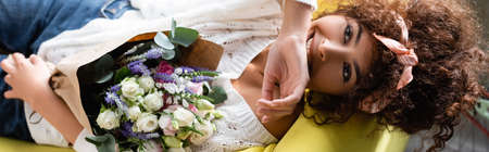 top view of curly woman with flowers laughing while lying on couch, panoramic shotの写真素材