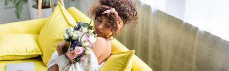 horizontal image of young woman with closed eyes holding bouquet and smelling flowers in living room