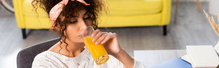 horizontal image of curly woman drinking fresh orange juiceの写真素材