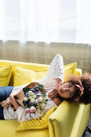 young curly woman lying on yellow sofa with flowersの写真素材