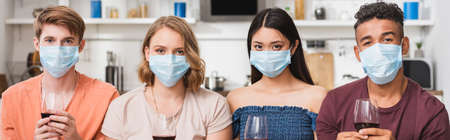 website header of multiethnic friends in medical masks holding glasses of red wine on party during...