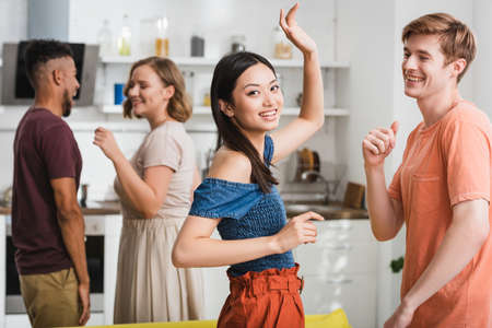 joyful asian woman looking at camera while dancing with multicultural friendsの写真素材