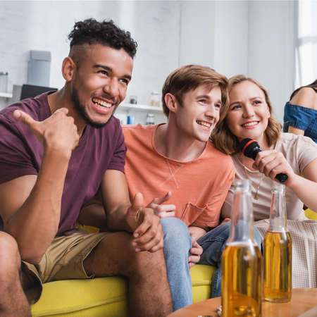 selective focus of excited african american man showing thumb up near multicultural friends singing karaokeの写真素材