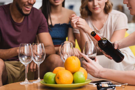cropped view of young man pouring red wine near fruits and multicultural friendsの写真素材