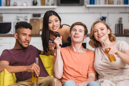 joyful multicultural friends singing karaoke during party