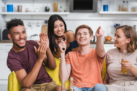 joyful african american man applauding while multiethnic friends singing karaokeの写真素材