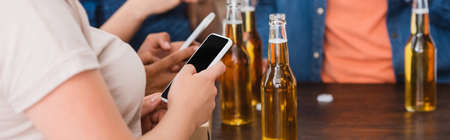 partial view of multiethnic friends chatting on smartphones near beer during party, horizontal cropの写真素材