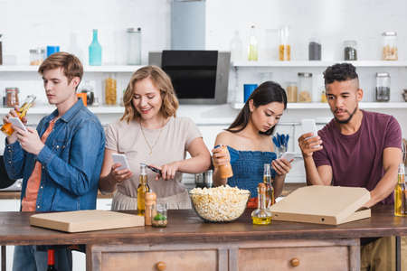 young multicultural friends chatting on mobile phones near beer and popcorn during party