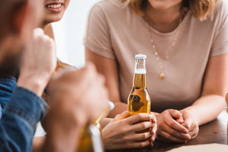 cropped view of woman holding bottle of beer near multicultural friendsの写真素材