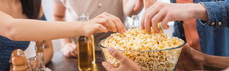 selective focus of multicultural friends taking popcorn from bowl during party, horizontal cropの写真素材