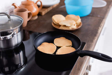 Selective focus of pancakes on frying pan on stove in kitchenの写真素材