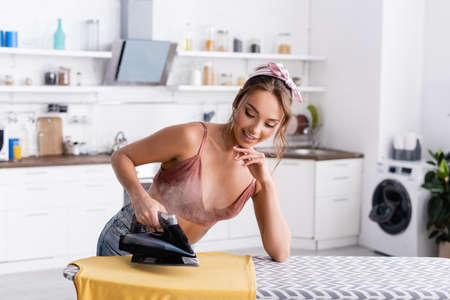 Young housewife ironing t-shirt with steam on ironing board at homeの写真素材