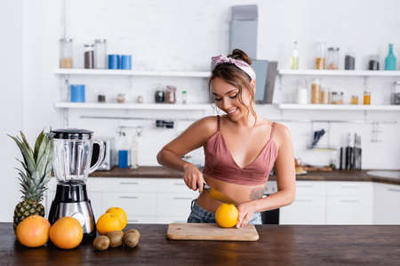 Young housewife cutting orange near fruits and blender on kitchen tableの写真素材
