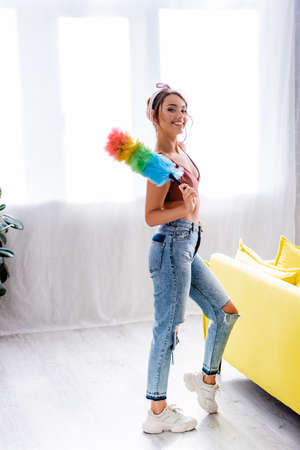 Housewife holding dust brush and looking at camera in living roomの写真素材