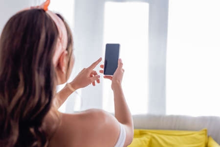 Selective focus of young woman using smartphone with blank screen at home
