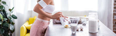Panoramic shot of young woman breaking eggs in bowl while cooking in kitchenの写真素材