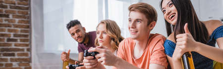 KYIV, UKRAINE - JULY 28, 2020: website header of asian woman holding beer and showing thumb up near friends playing video gameのeditorial素材