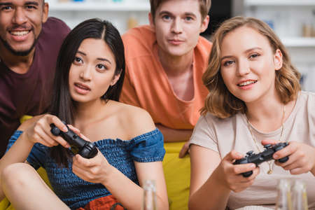 KYIV, UKRAINE - JULY 28, 2020: selective focus of concentrated multiethnic friends playing video game during partyのeditorial素材
