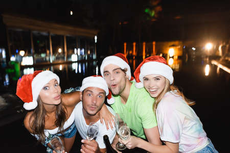 Friends in santa hats embracing while holding champagne and glasses during celebration new year at...