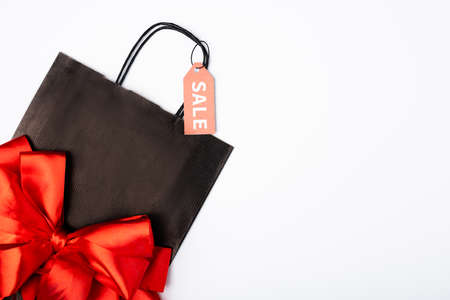 Top view of black shopping bag with bow and price tag with sale lettering on white background