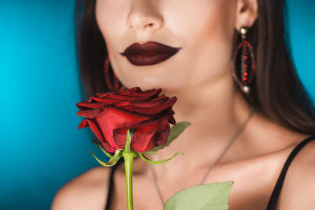 cropped view of woman with black lipstick near red rose on blue