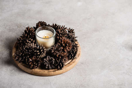 Scented candle with pine cones on wooden plate on gray and textured backgroundの写真素材