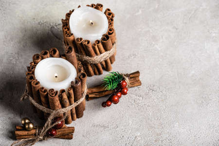Scented candles decorated with cinnamon sticks on gray and textured background