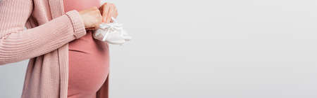 panoramic crop of pregnant woman holding baby boots isolated on white