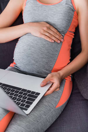 cropped view of pregnant woman in sportswear using laptop at homeの写真素材