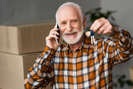 happy senior man talking on phone and holding keys in new house, moving concept