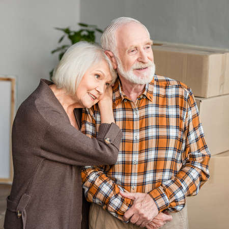 cheerful senior woman leaning on husband shoulder in new houseの写真素材