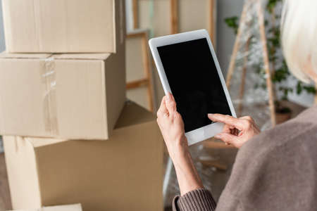 cropped view of woman holding digital tablet with blank screen with cardboard boxes on background, moving conceptの写真素材