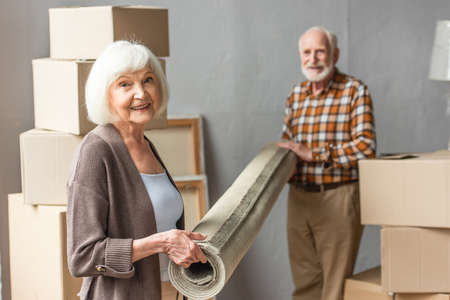 smiling senior couple rolling carpet in new house, moving conceptの写真素材