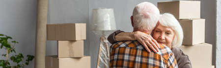 panoramic shot of senior woman with closed eyes hugging husband in new house, moving conceptの写真素材