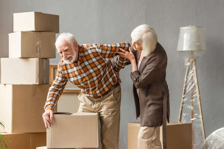 senior man suffering from backache and holding box while wife trying helpの写真素材