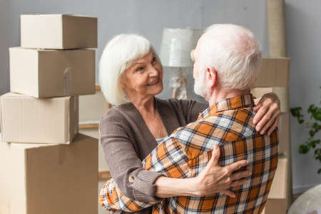 happy senior couple hugging and looking at each other in new houseの写真素材