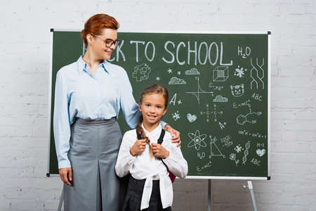 teacher and schoolgirl standing near chalkboard with back to school letteringの写真素材