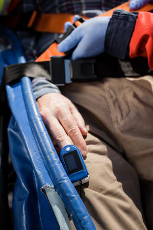 Cropped view of paramedic in latex gloves locking belt of stretcher near patient with heart rate...