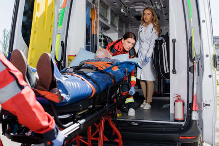 Selective focus of doctor standing near paramedics holding stretcher with patient in ambulance carの写真素材