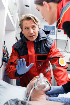 Selective focus of paramedic talking to colleague and showing stop gesture near patient in oxygen...
